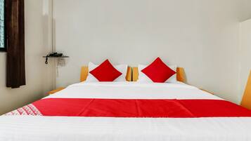 Een bed met een wit en rode sprei, twee rode kussens en een telefoon op een nachtkastje.