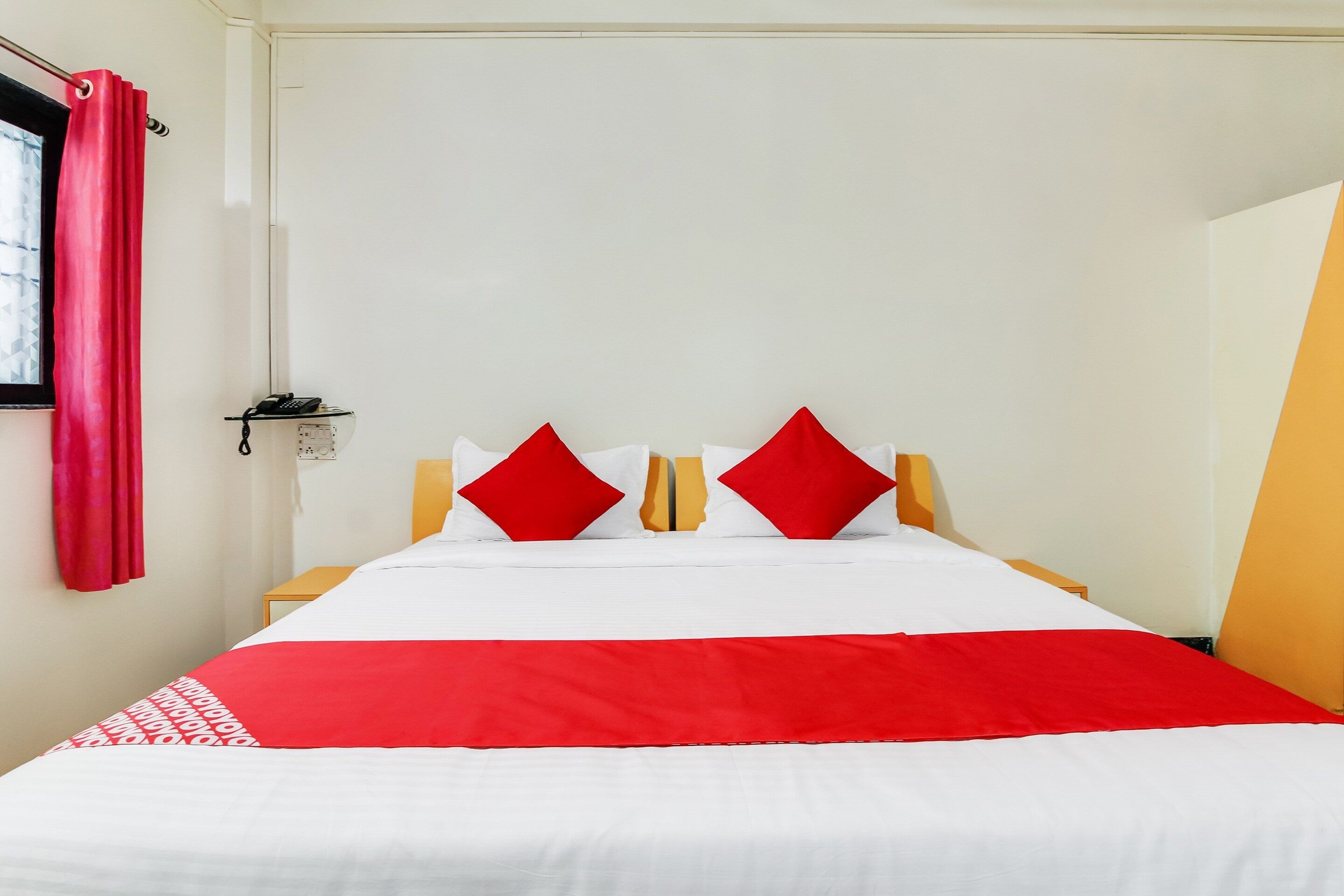 A bed with a red and white bedspread, two red pillows, and a telephone on a bedside table.