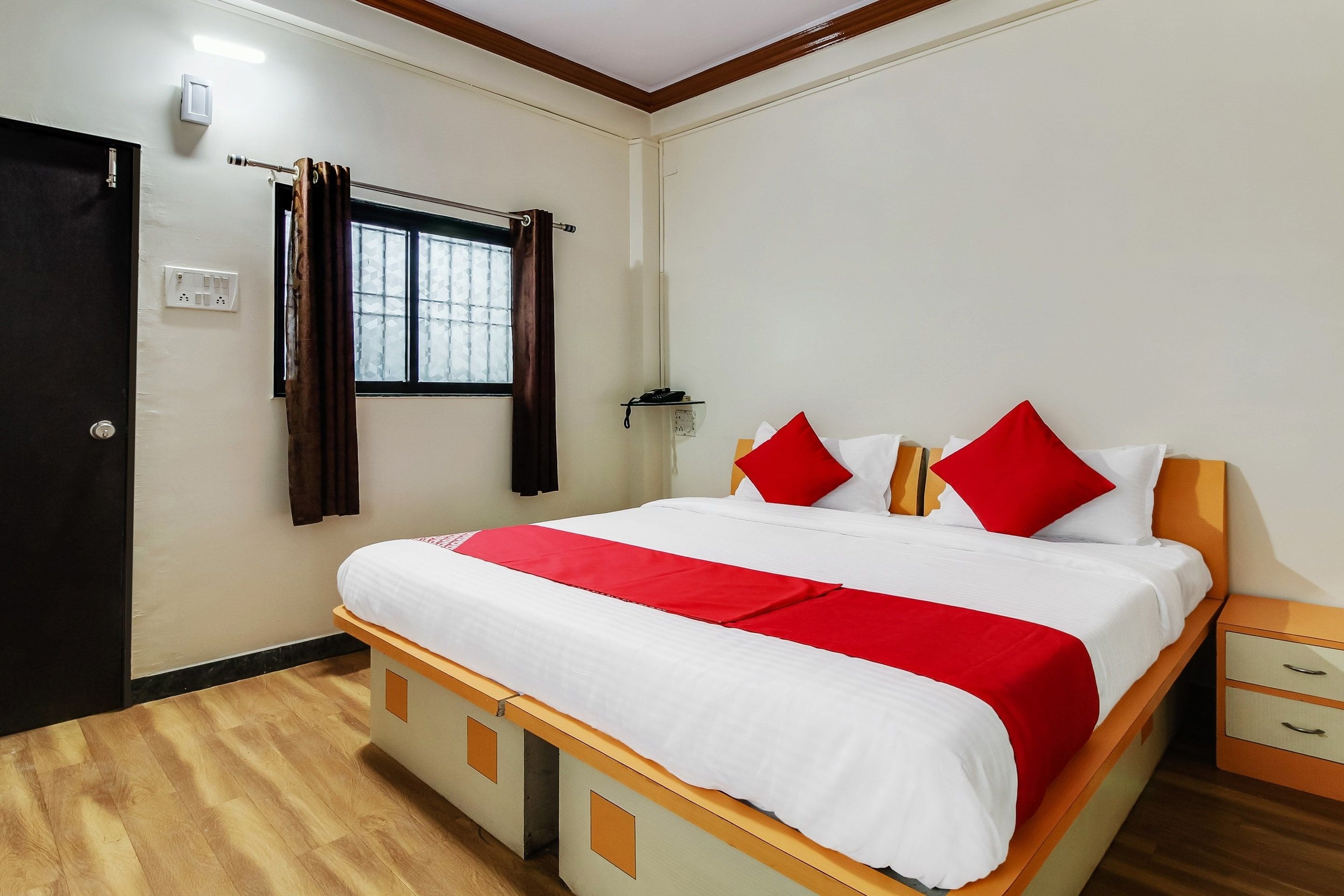 Een hotelkamer met een bed, nachtkastje, gordijnen voor het raam, een deur en een stopcontact.