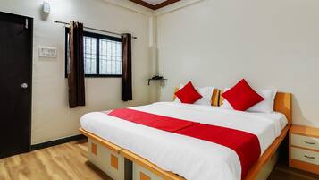Een hotelkamer met een bed, nachtkastje, gordijnen voor het raam, een deur en een stopcontact.