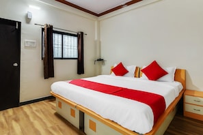 Quarto de hotel com cama, mesa de cabeceira, cortinas numa janela, porta e tomada na parede.