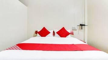 Een hotelkamer met een bed, twee rode kussens, een witte spreideken en een telefoon op een glazen plank.