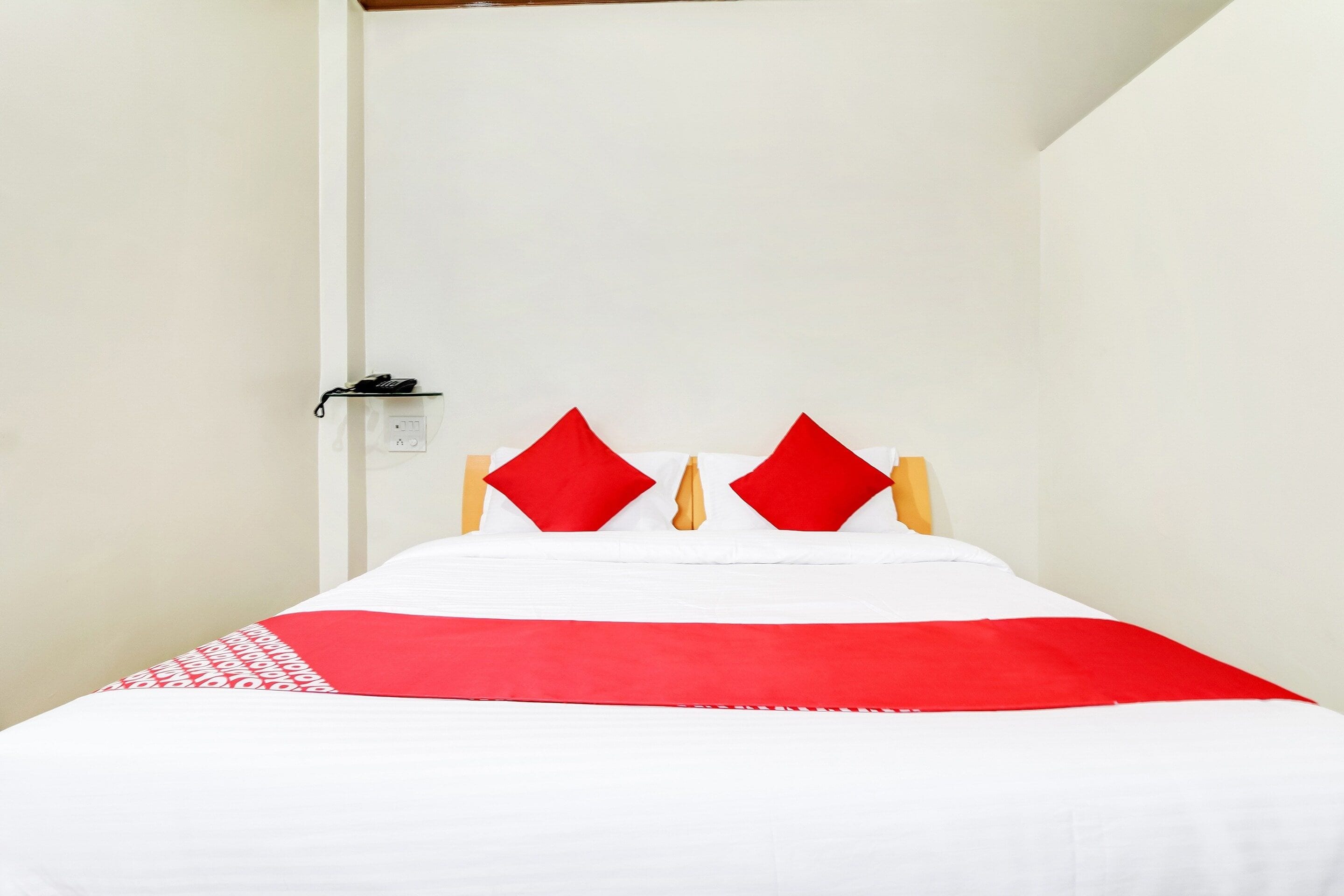A bed with a white and red bedspread, two red pillows, and a wooden headboard.