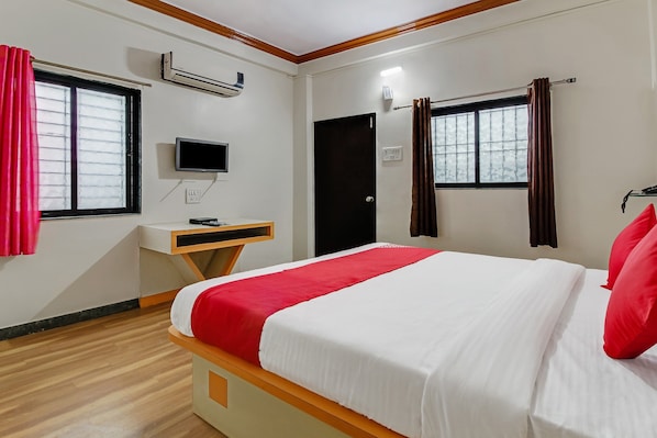 A hotel room with a bed, a desk, a TV, and a window with curtains.
