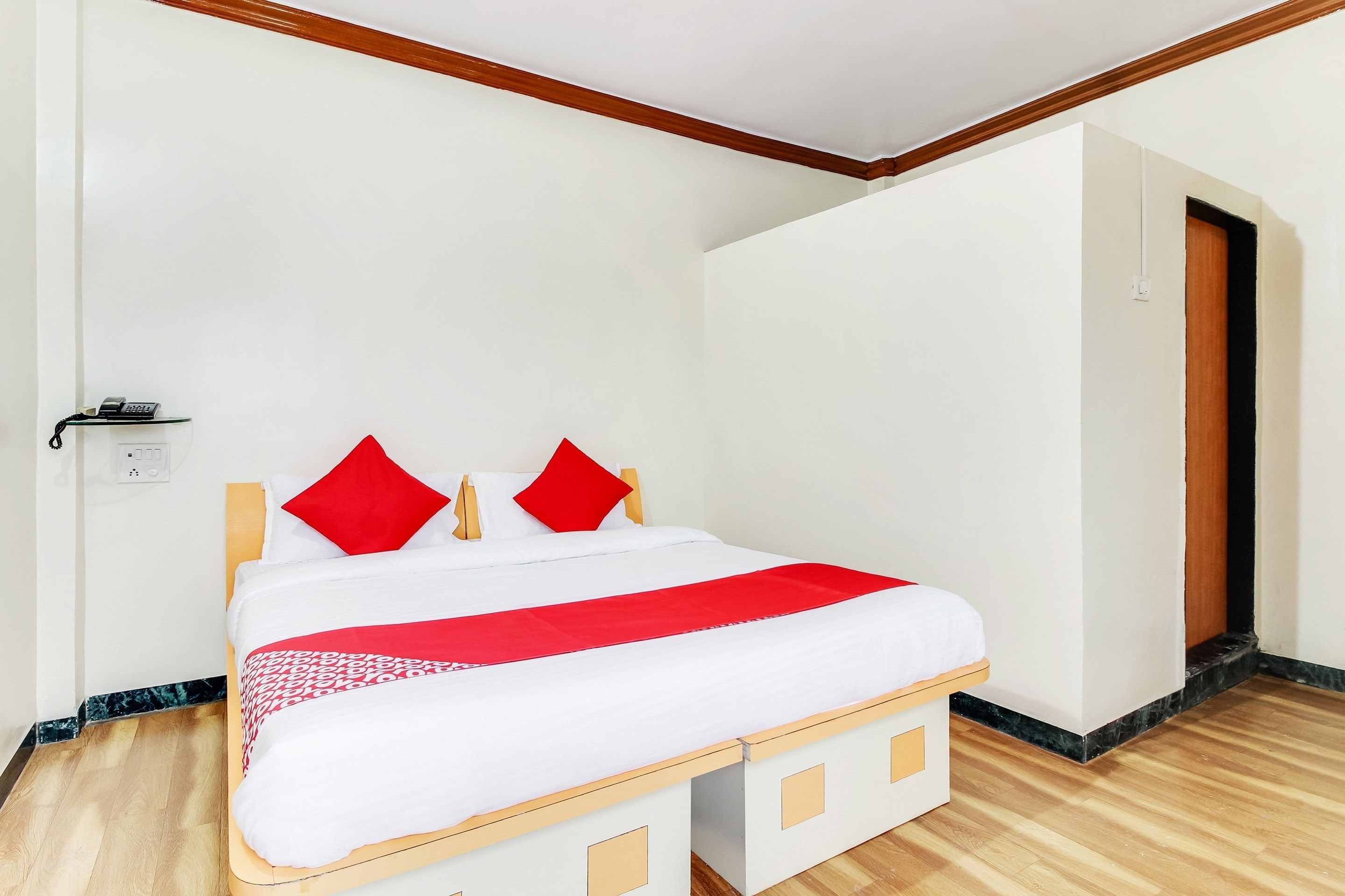A single-bed room with a wooden floor, white walls, and a door to the right.