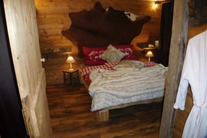 A wooden cabin-style bedroom with a large animal head headboard, a bed with red and white bedding, and two bedside lamps. - Chalet with private spa (Inzell)