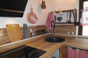 A kitchen with a wooden countertop, a sink, hanging kitchen utensils, and a window with a view. - Chalet with private spa (Inzell)