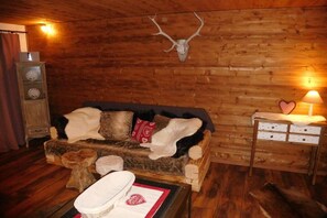 A rustic room with a wooden wall, a sofa with fur throws, a lamp, and a mounted deer skull. - Chalet with private spa (Inzell)