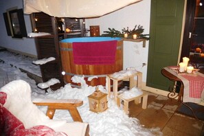 A cozy outdoor seating area with a wooden bench, a small table, and a wooden stool, surrounded by snow. - Chalet with private spa (Inzell)