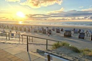 A beach with rows of beach chairs and umbrellas, a pedestrian walkway, and a sunset in the background. - Holiday apartment with 1 bedroom (Norderney)