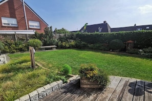 En bostadsträdgård med en gräsplätt, ett trädäck och ett hus byggt av tegel.