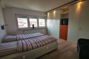 Ein Schlafzimmer mit zwei Betten, einem Fenster, einer Heizung, einem Kleiderschrank und einem Fernseher.