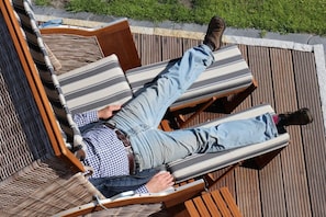 A person reclining on a wooden deck with striped cushions, a checkered shirt, and light-colored pants. - 4 House Achter de Duenen - the space miracle (Norderney)