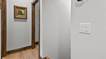 A hallway with a wooden floor, a framed picture on the wall, and a thermostat on the wall.