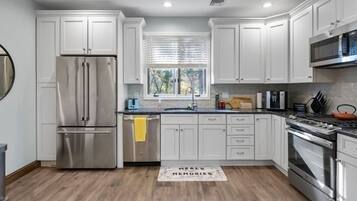 A modern kitchen with white cabinets, stainless steel appliances, and a wooden floor.