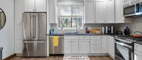 A modern kitchen with white cabinets, stainless steel appliances, and a wooden floor.