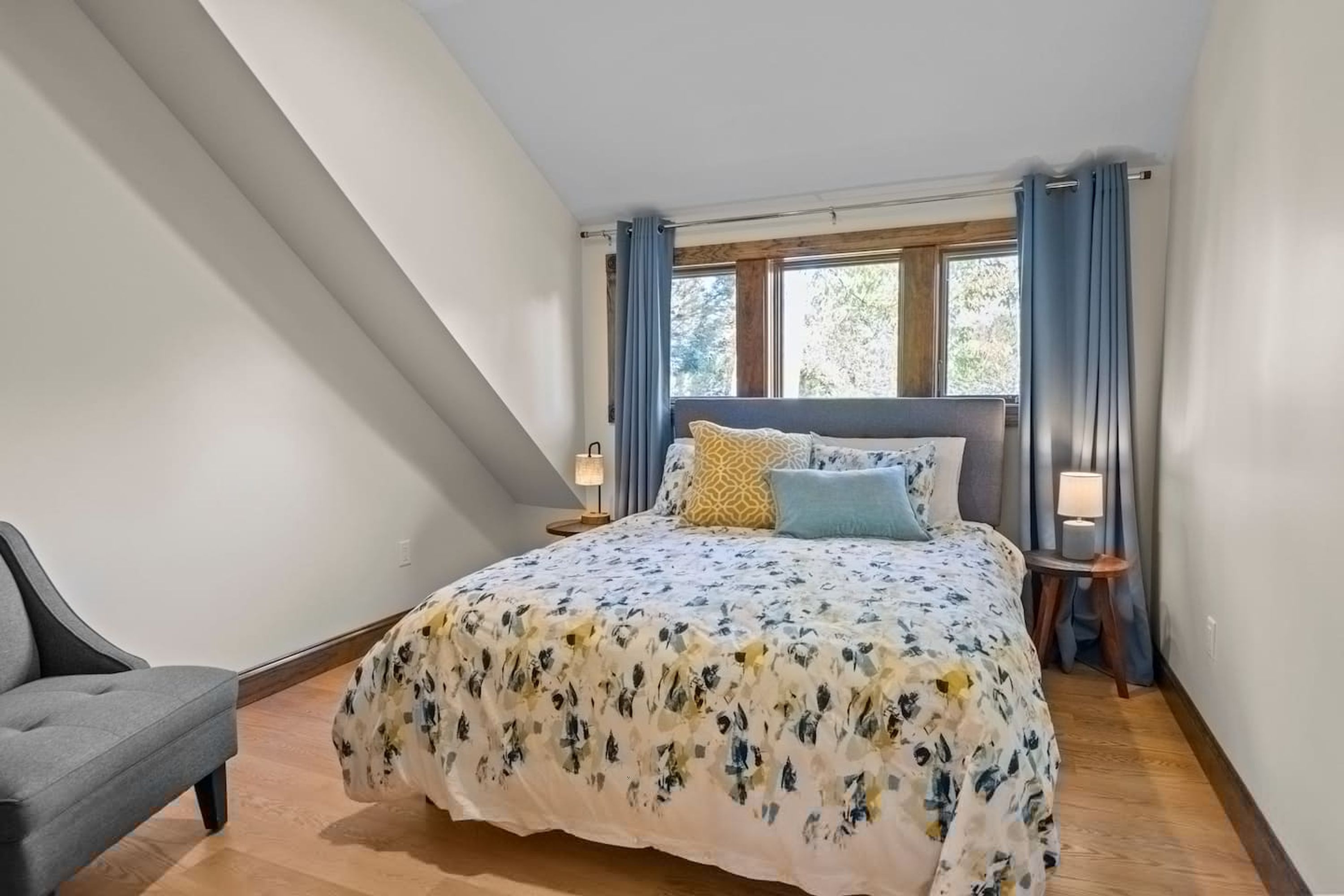 Un dormitorio con cama, una silla, ventana y cortinas.
