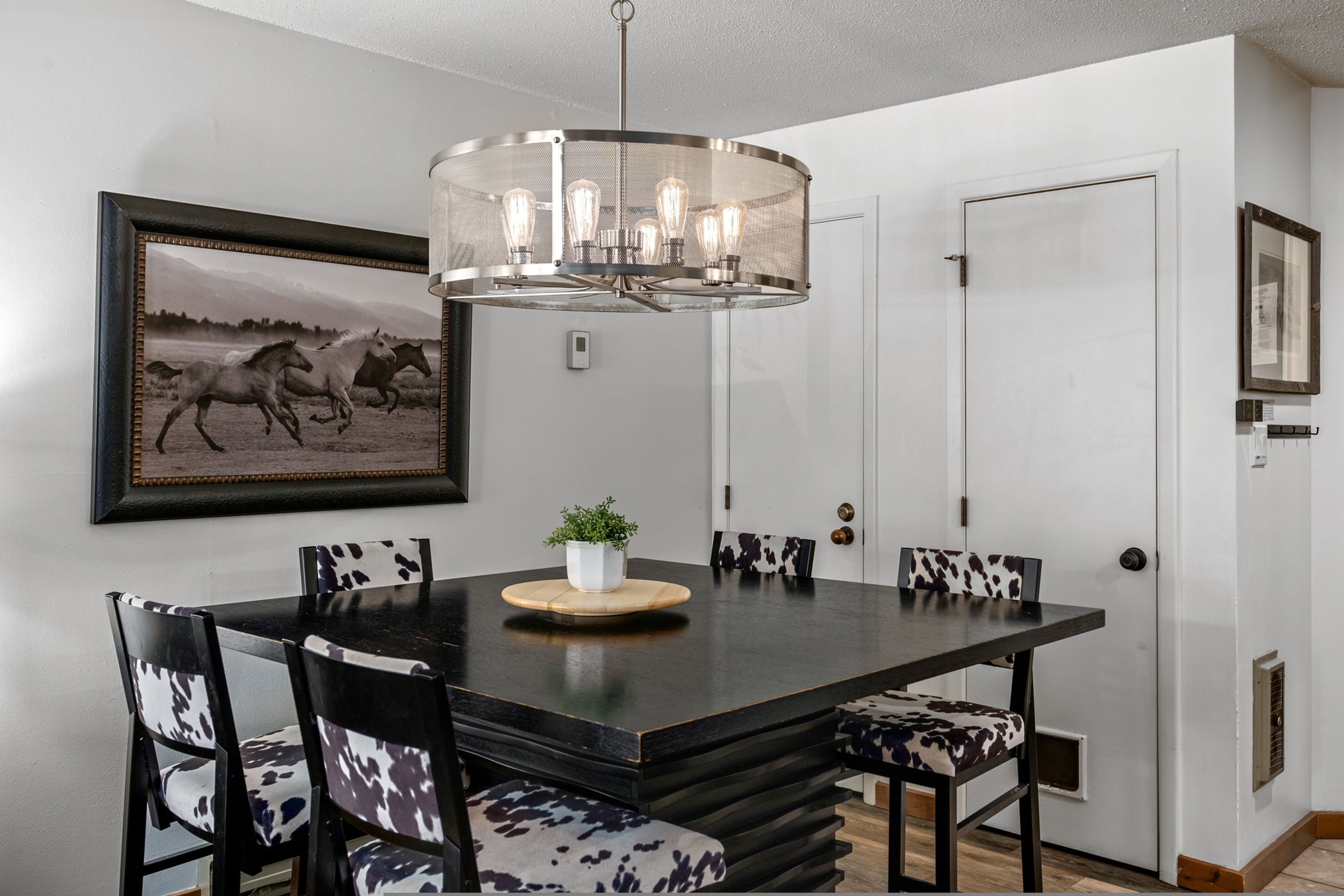 A dining area with a black table, patterned chairs, a chandelier, and a framed picture on the wall.