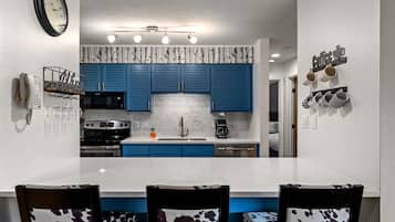Una cocina moderna con armarios azules, una encimera blanca y un comedor con dos sillas.