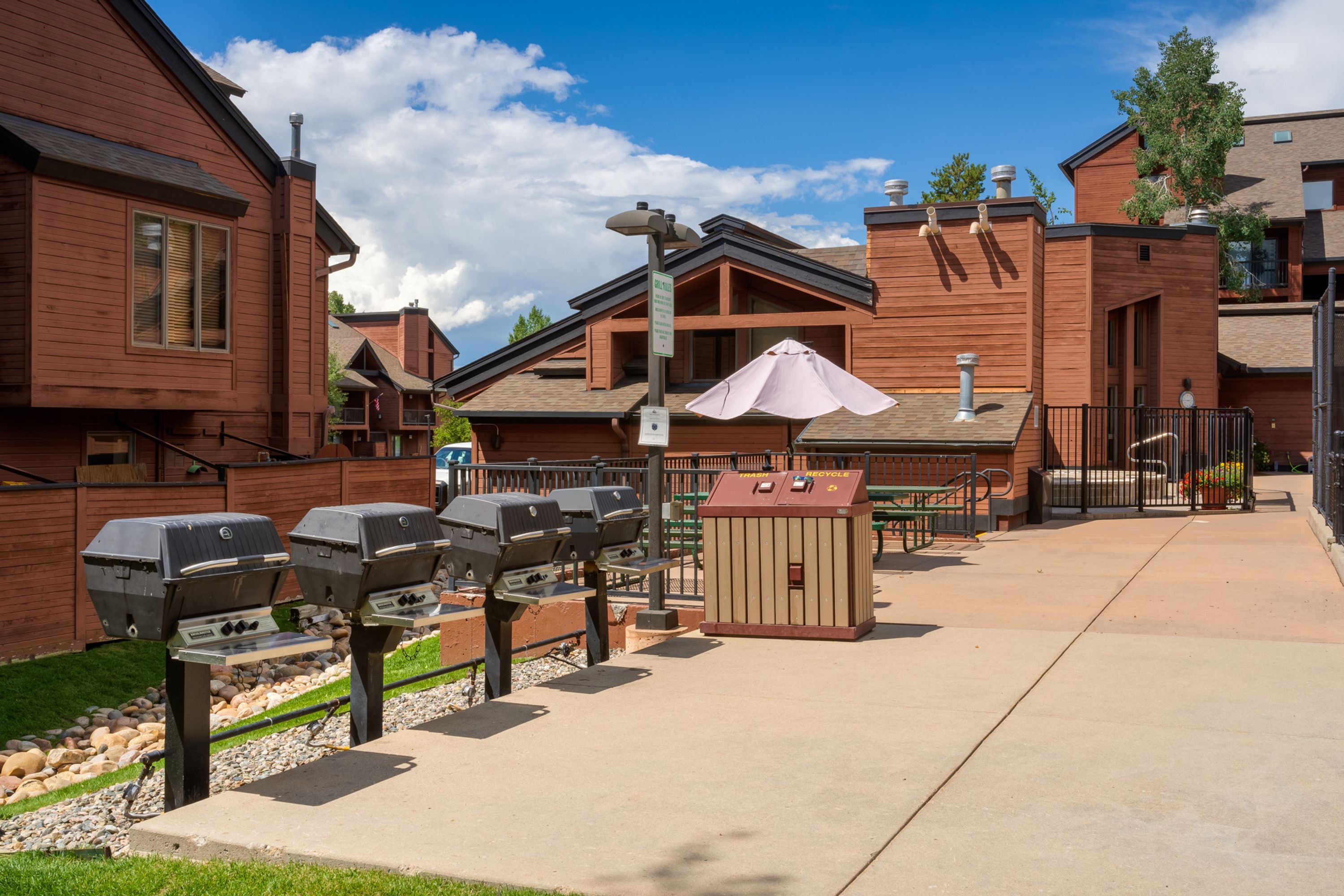 A patio area with barbecue grills, a trash and recycle bin, and a covered seating area.
