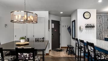 Un comedor con una mesa de madera, sillas con estampado blanco y negro, una lámpara colgante y un reloj de pared.