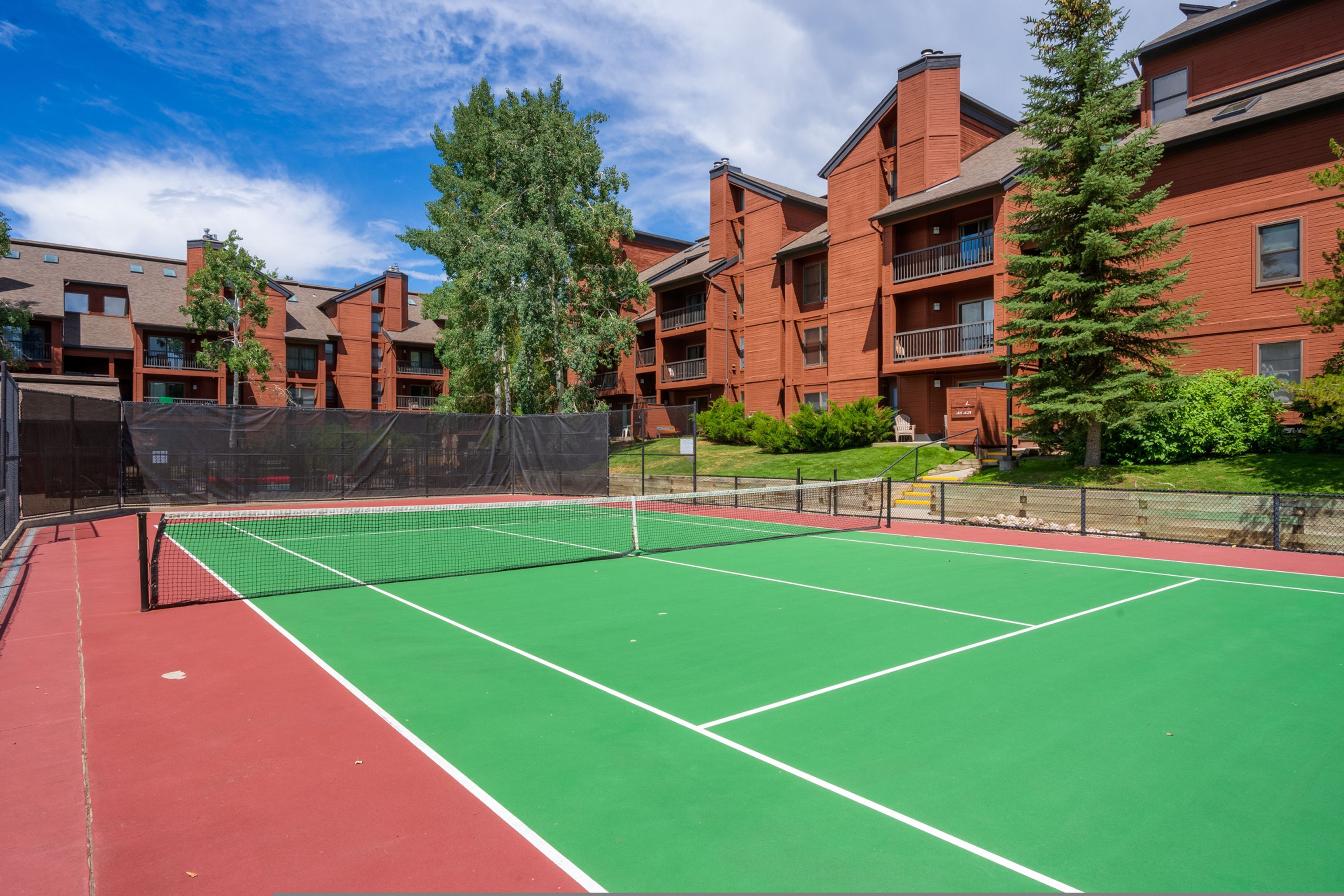 An outdoor tennis court surrounded by red brick buildings with balconies.