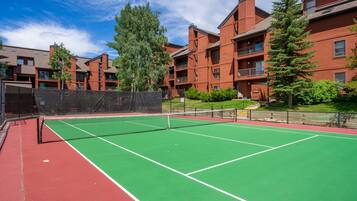 An outdoor tennis court surrounded by red brick buildings with balconies.
