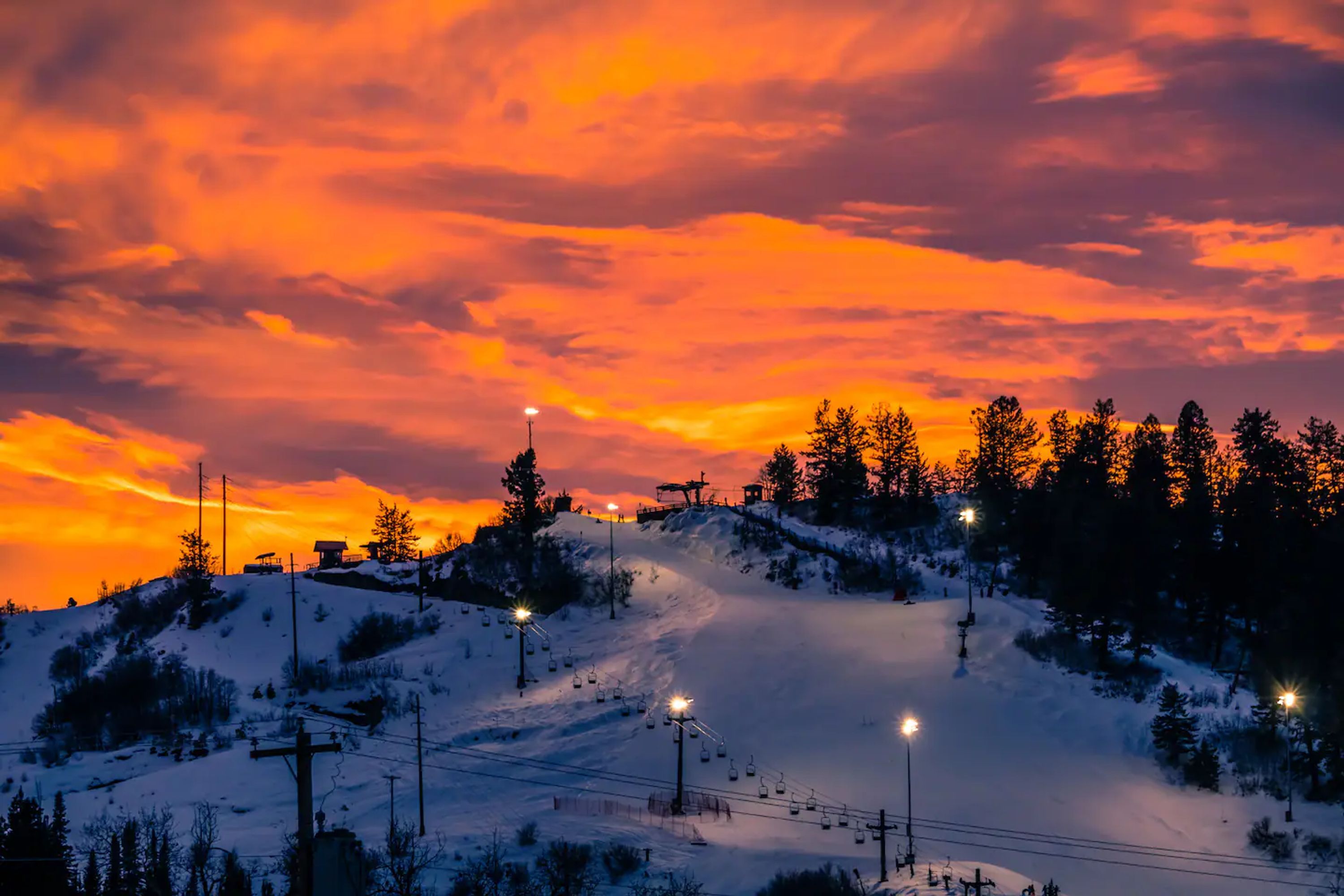 A snow-covered ski slope with ski lifts and a sunset sky.