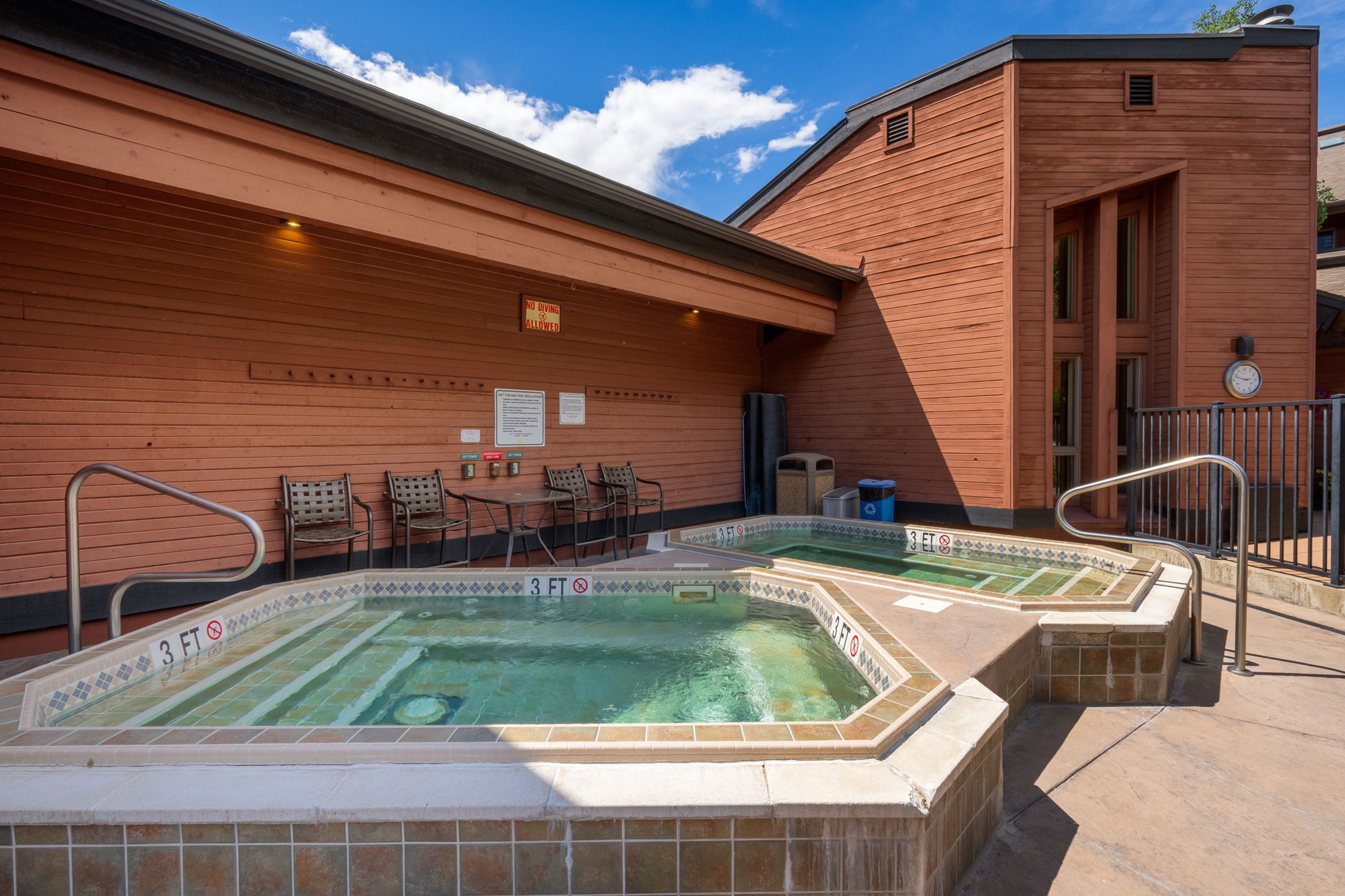 Zona de spa con bañera de hidromasaje y piscina, paredes de madera y asientos al aire libre.