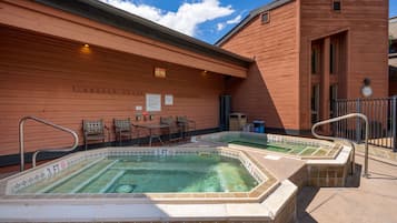 Zona de spa con bañera de hidromasaje y piscina, paredes de madera y asientos al aire libre.