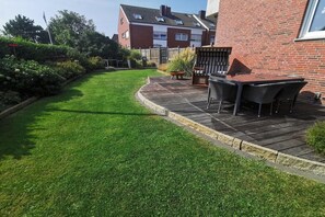 Een verzorgde tuin met een patio, een houten terras en een bakstenen muur.