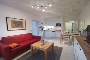 A compact living space with a red sofa, a wooden coffee table, and a kitchenette in the background. - Holiday apartment with 1 bedroom (Norderney)