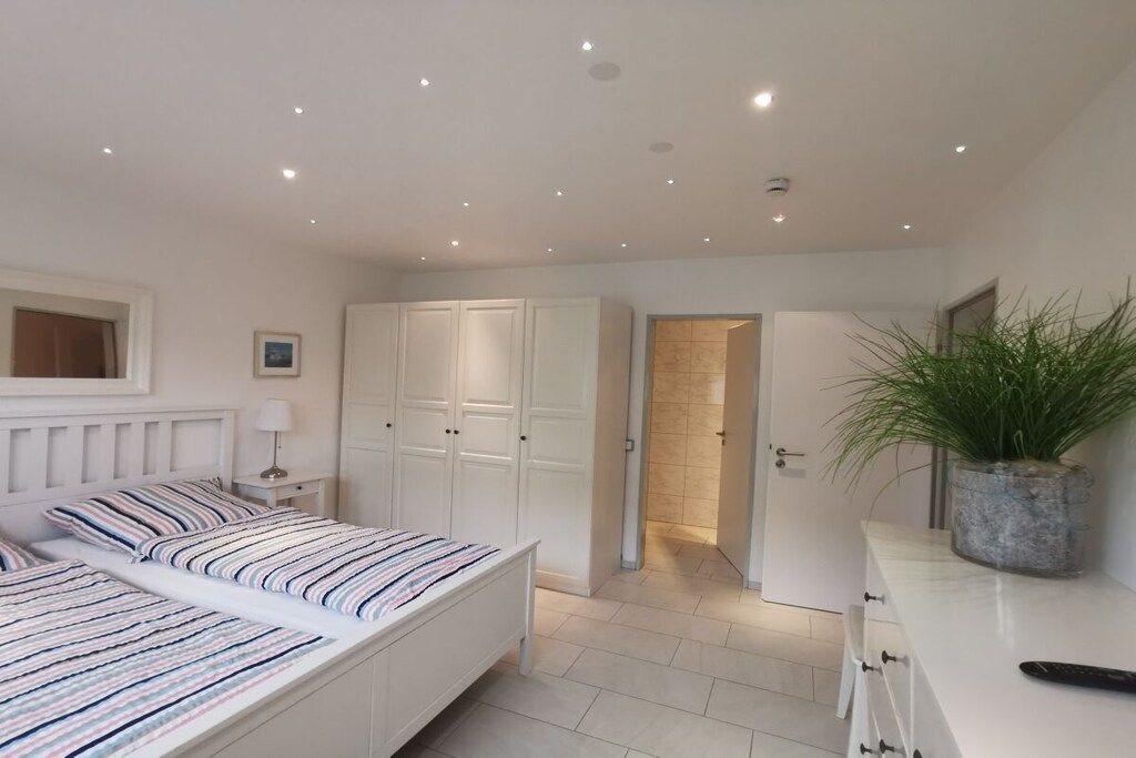 A bedroom with two beds, a wardrobe, a bedside table with a lamp, and a potted plant.