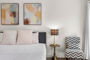 Ein Schlafzimmer mit einem Bett, Kissen, einer Nachttischlampe und einem Sessel.