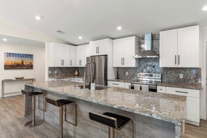 Eine moderne Küche mit weißen Schränken, Granit Arbeitsplatten, Edelstahlgeräten und einer Bar mit Hockern.