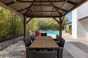 Ein überdachter Außenbereich mit einem Pool im Hintergrund.