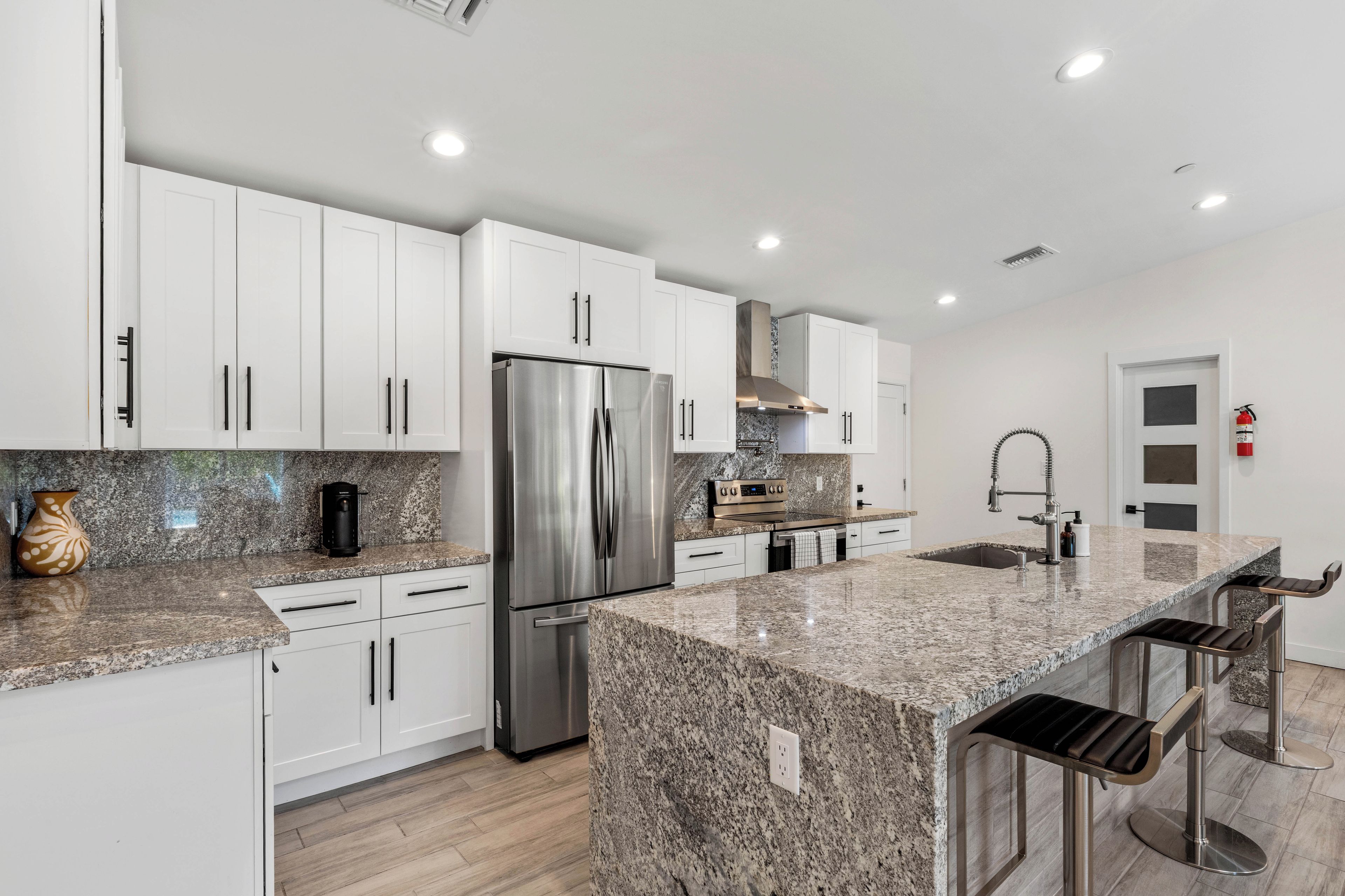 A modern kitchen with white cabinets, stainless steel appliances, granite countertops, and a bar area with stools.