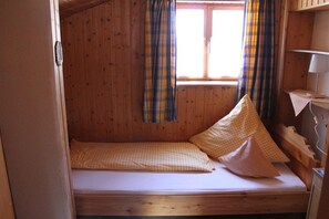 Ein kleines Zimmer mit einem Einzelbett, Holzvertäfelung und einem Fenster mit Karottenvorhängen.
