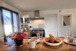 A modern kitchen with a stove, oven, and microwave. There is a dining table with a vase of flowers, a basket of croissants, and two wine glasses. - Villa in Brignogan Plages with barbecue (Brignogan Plages)