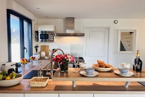 A modern kitchen with a built-in microwave, stainless steel range hood, and a large window. - Villa in Brignogan Plages with barbecue (Brignogan Plages)