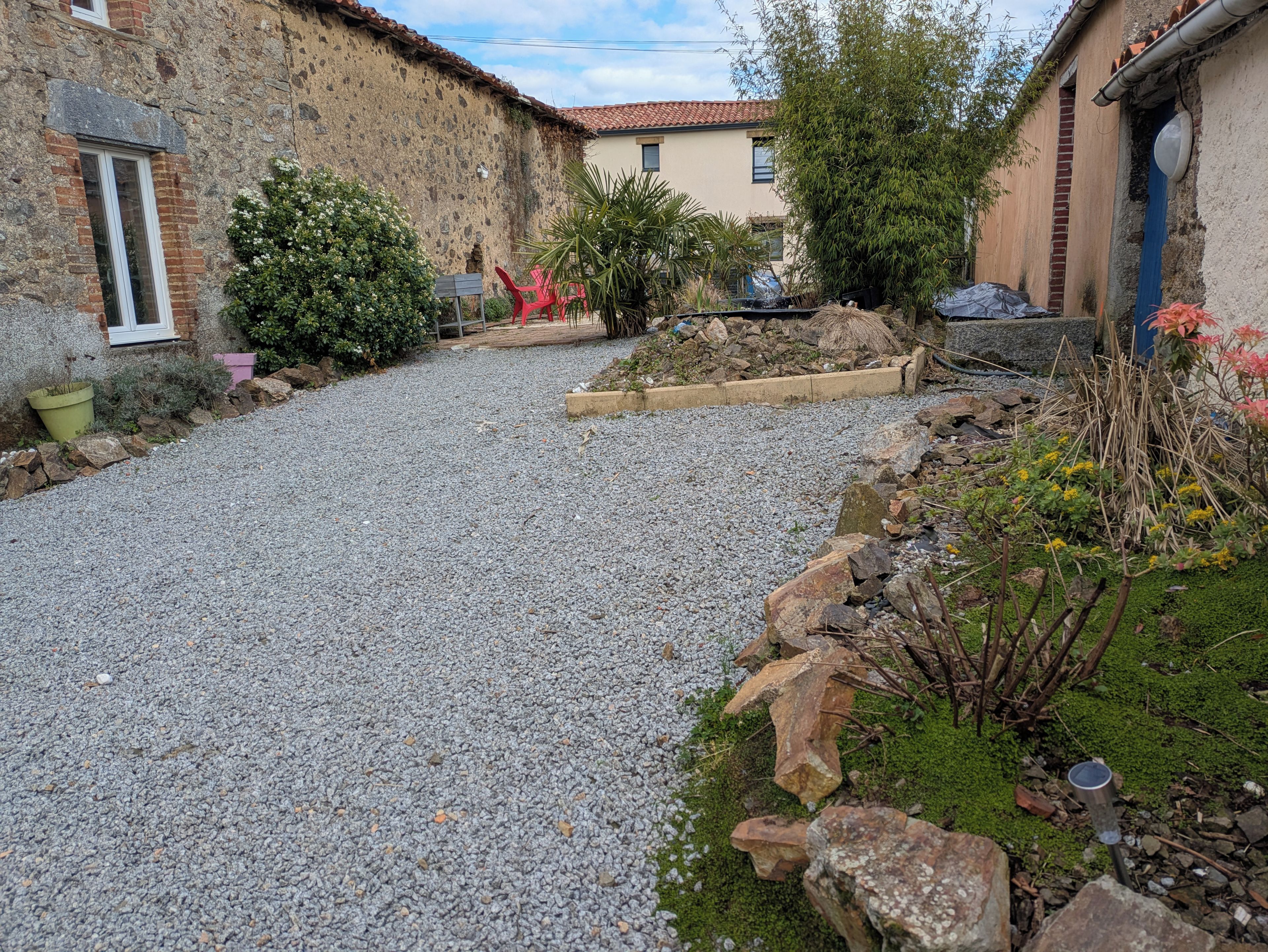 A gravel courtyard with stone walls, potted plants, and a small garden area.