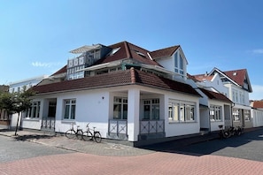 A two-story building with a red-tiled roof, white walls, and a covered porch area. - Vinkelau apartment 90m² with outdoor seating area (Norderney)