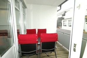 A small, enclosed balcony area with four red chairs and a white table. - Vinkelau apartment 90m² with outdoor seating area (Norderney)