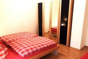 A bedroom with a bed, a wardrobe, and a red checkered bedspread. - Vinkelau apartment 90m² with outdoor seating area (Norderney)