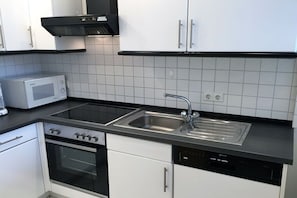 A modern kitchen with white cabinets, a black countertop, a built-in microwave, a stove, a sink, and a dishwasher. - Vinkelau apartment 90m² with outdoor seating area (Norderney)