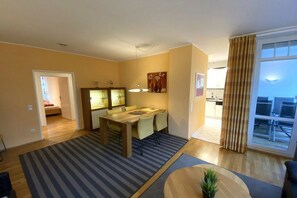Una sala de estar moderna con comedor, una cocina al fondo y un ventanal con cortinas.