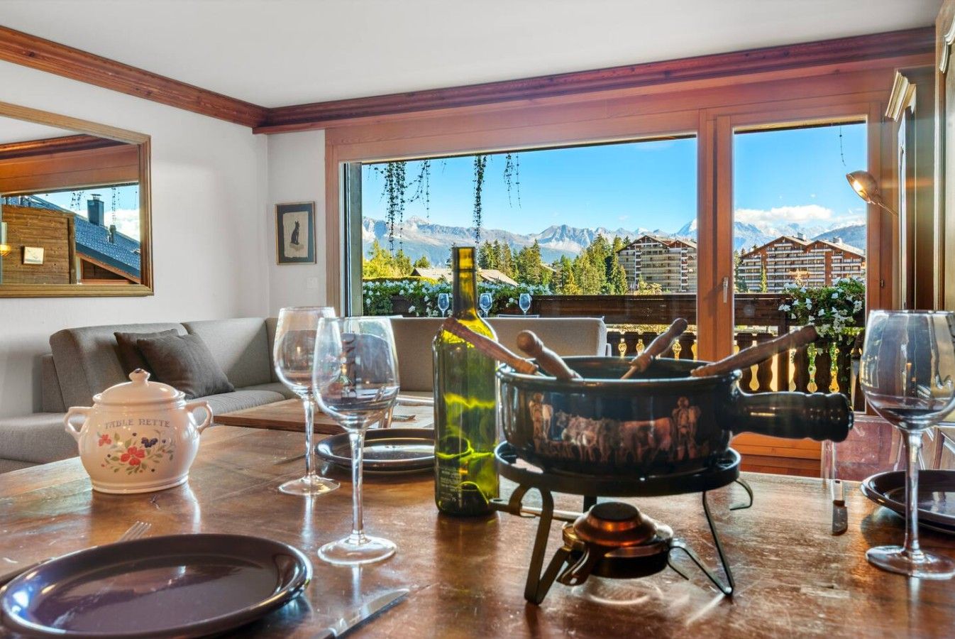 Un coin repas avec une table dressée pour deux personnes, une bouteille de vin, une théière et un réchaud portable.