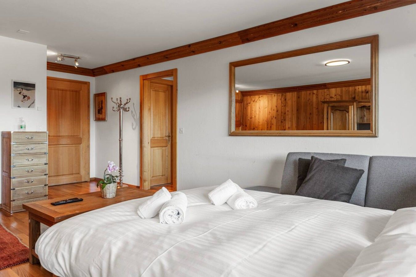 A bedroom with a large bed, a wooden dresser, a mirror, and a door.