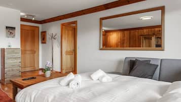 A bedroom with a large bed, a wooden dresser, a mirror, and a door.
