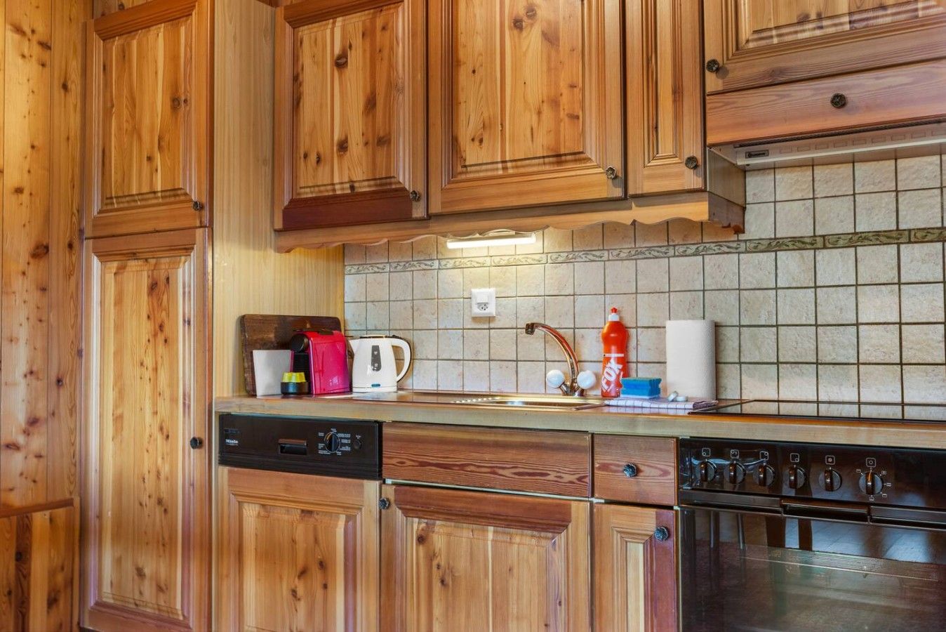 Een keuken met houten kastjes, een vaatwasser, een fornuis en een betegelde achterwand.